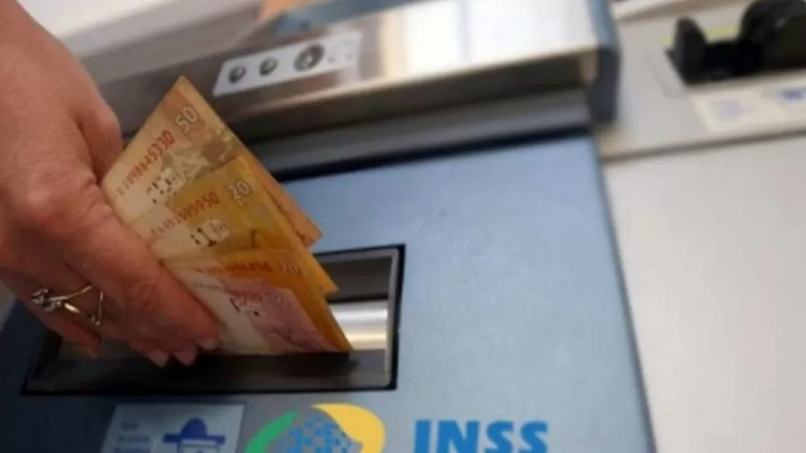 Pessoa insere notas de reais em máquina com logotipo do INSS, representando recebimento de benefícios previdenciários.