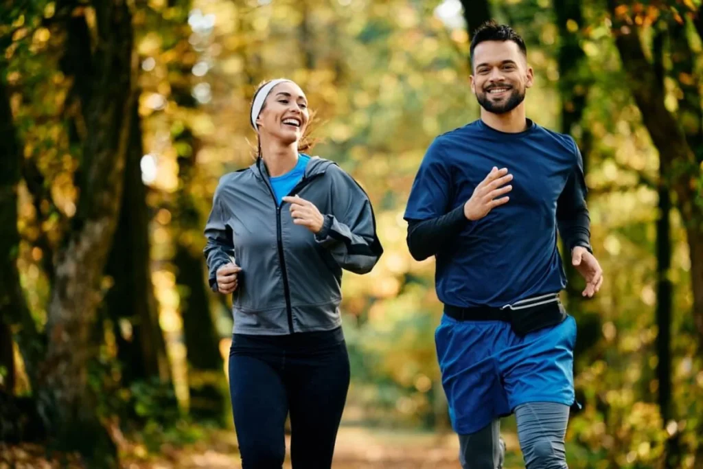 Duas pessoas praticando corrida em meio à natureza, vestindo roupas esportivas e aproveitando o ambiente arborizado.