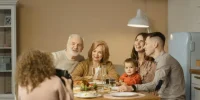  Família sorridente posa durante refeição festiva enquanto alguém registra o momento com uma foto.
