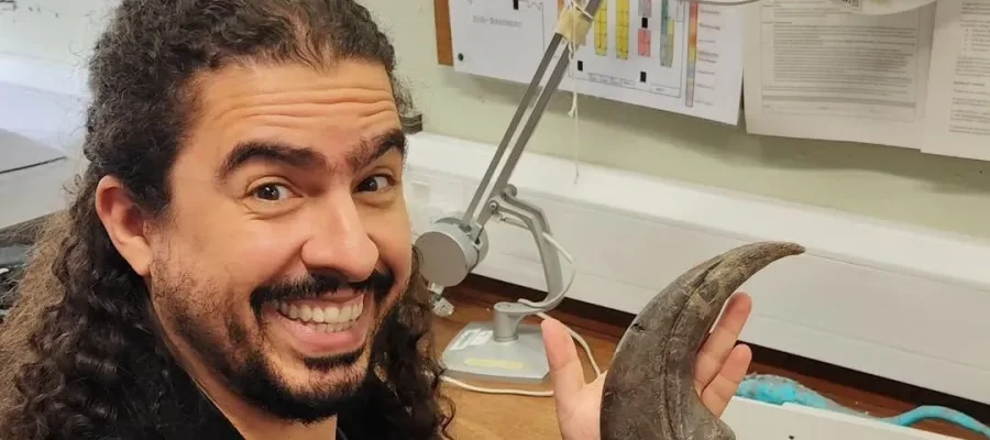 Após receber alta hospitalar, o biólogo e divulgador científico Pirulla retorna aos estudos com garra — literalmente. A imagem mostra o youtuber em seu ambiente de pesquisa, segurando uma impressionante garra fóssil.